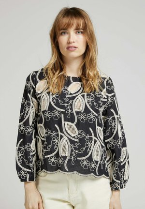 Blouse noire avec broderie florale et feuillage crème, un col rond et un ourlet festonné. Manches longues avec poignets froncés. Tissu léger.