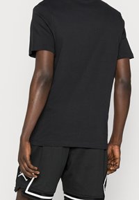 Camiseta de algodón negra con mangas cortas, cuello redondo, textura suave. Combinada con shorts de malla negra con acentos blancos y aberturas laterales.