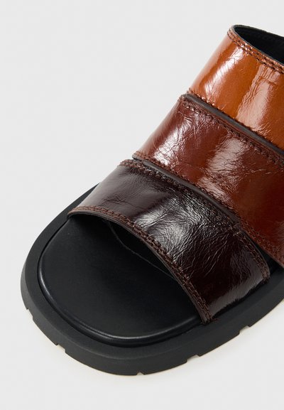 Καφέ δερμάτινο σανδάλι σλάιντ με τρεις επικαλυπτόμενους ιμάντες σε διάφορες αποχρώσεις. Υφή με ανάγλυφο φινί ρισμα και μαύρη καουτσούκ σόλα.