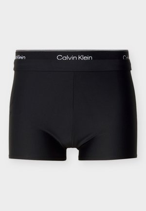 Schwarze Boxer-Shorts aus glattem Stoff, mit einem Calvin Klein Logo am Bund und einem anliegenden Schnitt. Einfach, ohne sichtbare Muster oder Verzierungen.