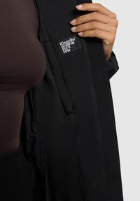 Fekete, könnyű dzseki cipzáros záródással, bal oldalon belül "KhuioTm Original for a Few" feliratú szövetcímkével.