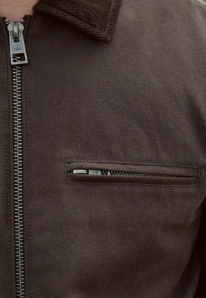Hnědá bunda s předním zipem a náprsní kapsou, vyrobená z texturované látky s ribbovým límcem a kovovými detaily.