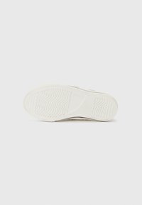Semelle de chaussure de sport blanche avec un fond en caoutchouc texturé présentant des motifs en vagues, un bout arrondi et une légère élévation au niveau du talon.