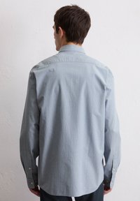 Chemise à manches longues rayée bleu clair et blanche avec un col boutonné, présentant une coupe décontractée et des manches à poignets.