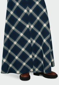 Larga falda a cuadros con una base azul marino y cuadrados en blanco, verde y gris. Combinada con botas marrones de suela resistente en la parte inferior.