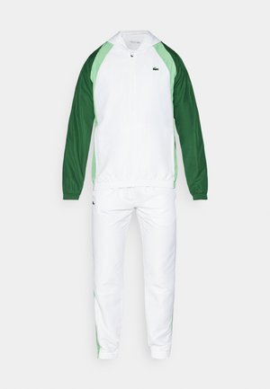 Chándal blanco con acentos verdes; chaqueta con cremallera que incluye una capucha, puños elásticos y pantalones a juego con paneles laterales verdes. Corte clásico.