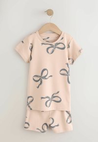 Ensemble beige pour tout-petit composé d'un haut à manches courtes et d'un short avec imprimés de nœuds gris, suspendu à un cintre en bois contre un mur blanc.