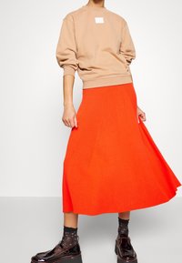 Sudadera beige con una pequeña etiqueta blanca, combinada con una falda naranja brillante de canalé hasta la rodilla y zapatos plataforma negros con calcetines con estampado.