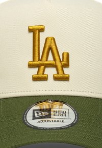 Verstellbare Baseballmütze mit einer cremefarbenen Oberseite und einem olivgrünen Schirm. Sie hat ein gesticktes goldenes "LA"-Logo und ein rundes New Era-Etikett darunter.