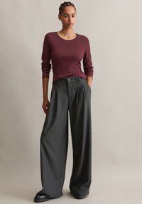 Bordeaux langermet topp kombinert med høyt liv, vide grå bukser, med knappdetalj og sidelommer, laget av glatt stoff.