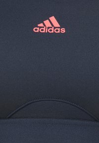 Sutiã desportivo azul-marinho com um tecido texturizado, apresentando uma secção frontal central e um logótipo da adidas em rosa brilhante no canto superior esquerdo.