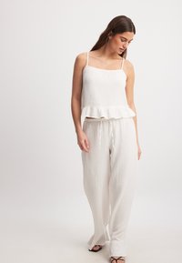Weißes Baumwolltanktop mit einem gerafften Saum, kombiniert mit locker sitzenden, verstellbaren Hosen. Beide Teile haben eine strukturierte Oberfläche und eine lässige Silhouette.