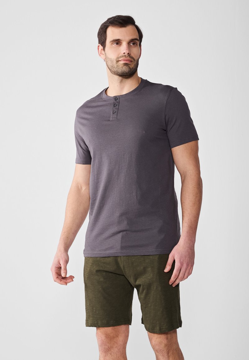 Graues Kurzarm-T-Shirt mit Rundhalsausschnitt und dreiknopf-Button-Down, kombiniert mit dunkelgrünen Shorts aus strukturiertem Stoff.