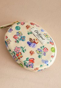 Ovale tas van crème stof met een bloemmotief, voorzien van een rits en een stoffen label met de opdruk "Cath Kidston London".