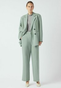 Lysegrønn skreddersydd dress med dobbelspent blazer og bukser med rette ben, kombinert med en grå turtleneck og spisse kremfargede hæler.