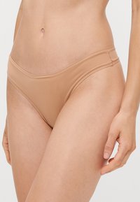 Beige naadloze bikini slip met een lage taille, een gladde textuur en subtiele stiksels langs de tailleband en beenopeningen.