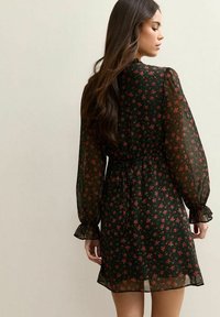 Robe noire à motifs floraux rouges, en tissu transparent, avec de longues manches puff à poignets volantés et une silhouette cintrée.