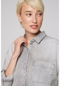 Light gray button-up shirt with a classic collar, roll-up sleeves, and a front pocket. Smooth fabric with a soft texture.