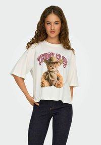 Biała koszulka z krótkim rękawem z grafikiem przedstawiającym misia w czapce, z napisem "Teddy Club" w kolorze czerwonym powyżej. Luźny krój i miękki materiał.