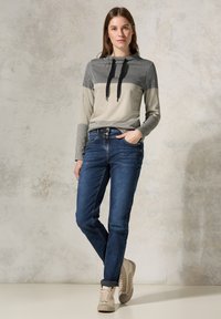 Gestreepte, hooded top in grijs en zwart met zwarte trekkoorden; gecombineerd met blauwe jeans en beige sneakers. Eenvoudige, casual outfit.