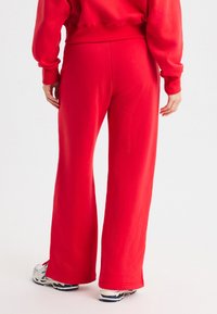 Rote Jogginghose mit weitem Bein und elastischem Bund, aus weichem Stoff gefertigt. Kombiniert mit einem passenden roten, kurzen Sweatshirt und sportlichen Schuhen.