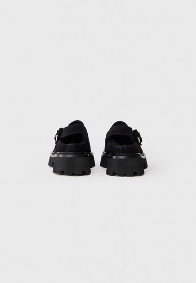 Zapatos de plataforma de ante negro con suelas de goma gruesas, que cuentan con parte trasera abierta, dos correas y acentos de hardware metálico.