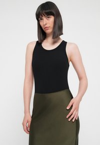 Black ribbed tank top paired with a sleek olive green skirt. The top features a classic round neckline and shoulder straps.