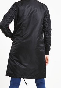 Czarny, długi płaszcz z długim rękawem, wykonany z błyszczącego materiału, o długości do środka uda, z prążkowanymi mankietami i regulowanym ściągaczem na dole.