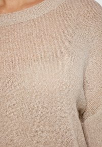 Pulover tricotat bej, cu o croială lejeră, decolteu larg și un material texturat. Manșetele și tivul ribbate accentuează designul său relaxat.