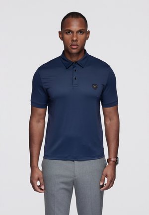 Granatowa koszulka polo z zaostrzonym kołnierzykiem, pliską na trzy guziki i małym czarnym logo na piersi. Materiał wydaje się gładki i dopasowany.