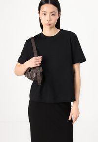 T-shirt noir à manches courtes avec une coupe décontractée, en coton, associé à un petit sac à main en cuir brun foncé. Design simple et minimaliste.
