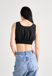 Haut court noir avec un col rond et une taille élastique ; porté avec un jean taille haute bleu clair orné d'une étiquette de marque rouge.