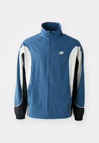 Blå, hvit og svart New Balance zip-up sportsjakke med høy krage og elastiske mansjetter, vist på en enkel hvit bakgrunn.