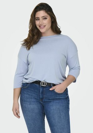 Light blue, lightweight, long-sleeve top with a loose fit. Paired with dark blue denim jeans and a black belt featuring a silver double-circle buckle.
