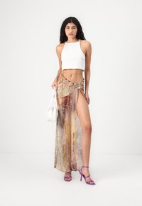White cropped tank top, sheer long skirt with abstract orange and brown patterns, embellished with a decorative belt, paired with purple heels.