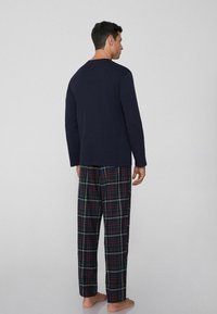 Granatowa bluzka z długim rękawem zestawiona z spodniami w kratę w kolorach granatowym, zielonym, czerwonym i żółtym. Miękki materiał, luźny krój i lekka konstrukcja.