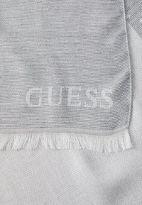 Hele hall harjaste tekstuuriga helehall sall, millel on reliefne sõna "GUESS". Servas on lühikesed ääred.