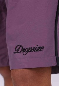 Fioletowe szorty z czarnymi akcentami na bokach i haftowanym logo "Dropsize". Materiał wydaje się lekki o gładkiej teksturze.