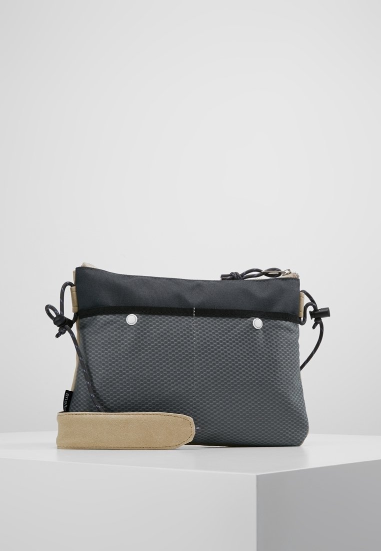 Czarna i beżowa torba z fakturowanego materiału, z zamknięciem na sznurku oraz srebrnymi akcentami. Prostokątny kształt z miękkim uchwytem.