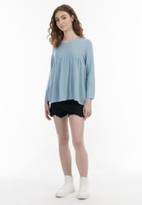 Lyseblå, tekstureret top med lange ærmer og samlet talje, parret med sorte cut-off shorts og hvide høje sneakers.