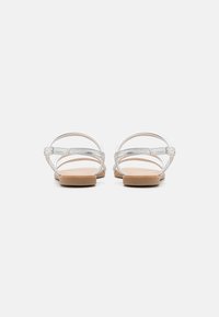 Silver flat sandals with multiple thin straps, a smooth footbed, and a light wood-like sole, featuring a buckle closure at the ankle.