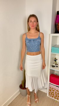 Τζιν crop top με ασημένιες καρφίτσες, συνδυασμένο με μια λευκή, φουσκωτή φούστα. Το σύνολο έχει στενή εφαρμογή και λεπτές τιράντες στους ώμους, συμπληρωμένο από λευκά σανδάλια.