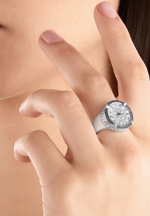 Mano con unghie naturali che indossa un anello d'argento con un design rotondo di bussola sul dito medio vicino al volto.