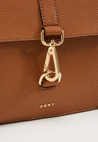 Borsa a mano in pelle marrone a superficie pebbled con chiusura in tonalità oro e marchio DKNY. Texture liscia con un design strutturato e chiusura sicura.