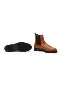 Botas de tobillo de cuero marrón con paneles laterales de elastano negro, puntera redondeada, una lengüeta y una suela de goma texturizada con agarraderas circulares.