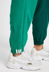 Gröna träningsbyxor med elastiska mudd på anklarna och siddragkedjor, tillsammans med klumpiga vita sneakers med meshoverk och släta läderdetaljer.