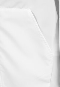 Tela blanca con una sutil textura en cuadrícula, que presenta un solo bolsillo en ángulo en el lado izquierdo y costuras limpias. Apariencia suave en general.