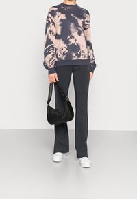 Sweatshirt tie-dye in rosa e blu navy, abbinato a pantaloni svasati scuri. Accessoriato con una piccola borsa a tracolla nera e sneakers bianche.