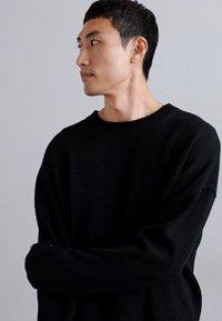 Pull noir en maille avec un col rond, coupe ample et manches longues. La texture est côtelée et le design est simple et minimaliste.