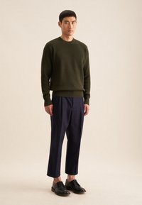Pull à côtes olives, pantalon large bleu marine et chaussures à lacets noires. Design simple avec une finition texturée et une coupe décontractée.